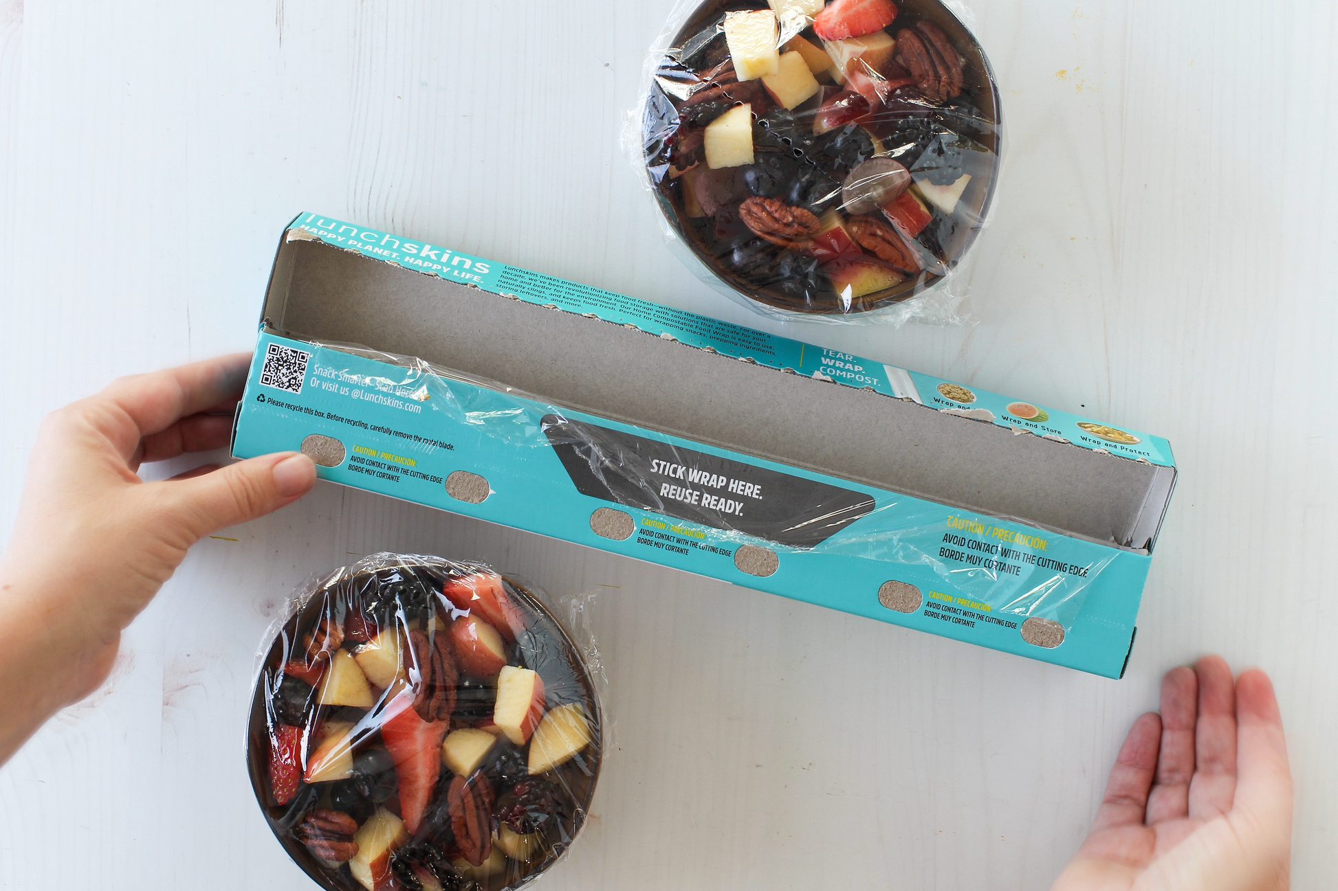 Hands opening a box containing a fruit  with a visible brand logo. Showing Reuse Ready Tab Lunchskins Food Wrap