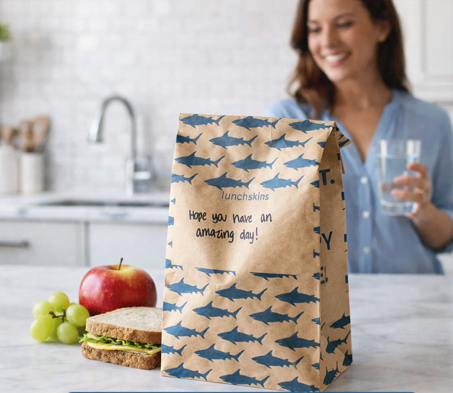 Image of Lunch bag with shark pattern and message, placed on a kitchen counter with an apple, grapes, and sandwich.